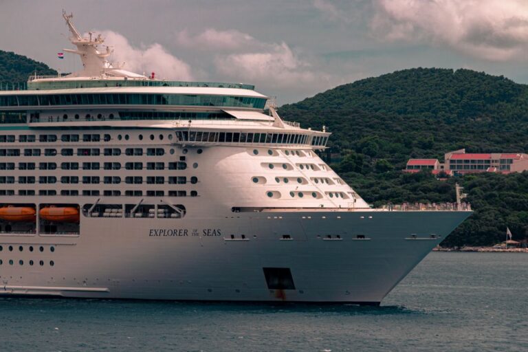 Large cruise ship 'Explorer of the Seas' navigating near lush green hills under a cloudy sky.