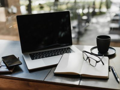 Workspace setup featuring a laptop, notepad, glasses, and coffee cup for productivity.